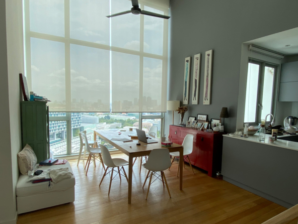 A well-lit dining area with large windows offering a panoramic cityscape, featuring a mix of modern and vintage decor elements. Nestled on a high floor, this dining space serves as an urban retreat, boasting a stunning view of the city skyline through floor-to-ceiling windows. The room is bathed in natural light, enhancing the warm wooden floors and the soft grey tones of the walls. A rustic, long wooden table paired with modern white chairs offers a harmonious blend of the old and new, while eclectic decor such as a vibrant red sideboard and sleek kitchen countertops reflects a personalized touch. Abstract art adorns the walls, adding an air of sophistication. This dining area is not just a place to eat but a serene spot to relish the city's pulse without the bustle, perfect for contemplative mornings or lively dinner parties at dusk.