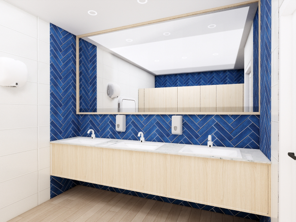 A stylish female washroom interior showcasing a large mirror, white sinks with modern fixtures, and vibrant blue herringbone tiles contrasted with light wooden cabinetry. This female washroom interior combines elegance and modern design. The eye is immediately drawn to the vibrant blue herringbone tiles that adorn the wall, providing a dynamic backdrop to the sleek white sinks. Above, a large, frameless mirror spans the length of the vanity, reflecting the well-lit space and amplifying its airy feel. Modern fixtures in clean lines are mounted onto the wall, maintaining the contemporary aesthetic. Below, the light wooden cabinetry brings warmth to the room, softening the boldness of the tiles and complementing the neutral tones of the flooring. This design is not only visually pleasing but also serves to create an inviting and comfortable space for its users.